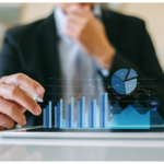 A professionally dressed individual sits at a well-lit desk analyzing printed charts, writing in a notebook, and using a laptop—highlighting the process of uncovering valuable fundraising data insights.